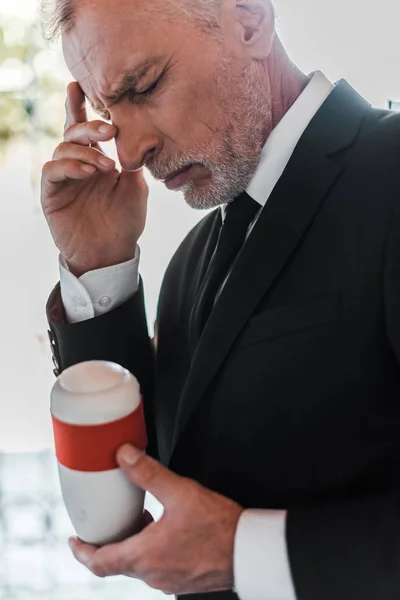 Selective focus of upset elderly man touching face and holding mortuary urn — Stock Photo