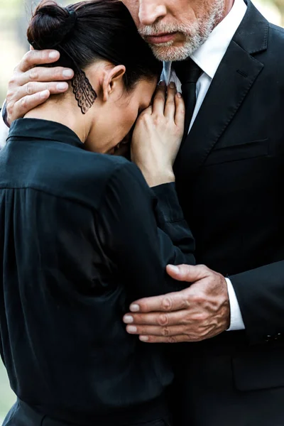 Обрезанный вид расстроенного пожилого мужчины обнимающего женщину на похоронах — стоковое фото
