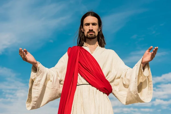 Бородатый Иисус с распростертыми руками против голубого неба — стоковое фото
