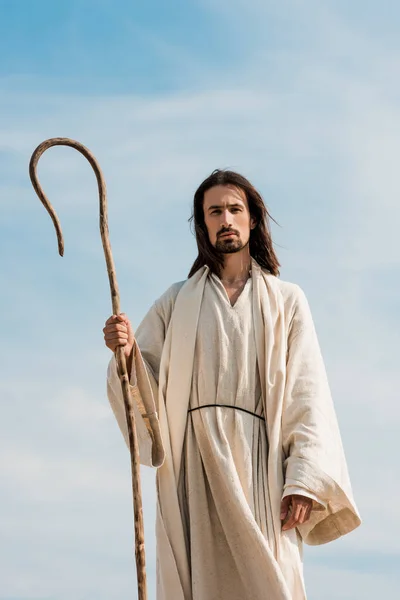 Man in jesus robe holding wooden cane against blue sky in desert — Stock Photo