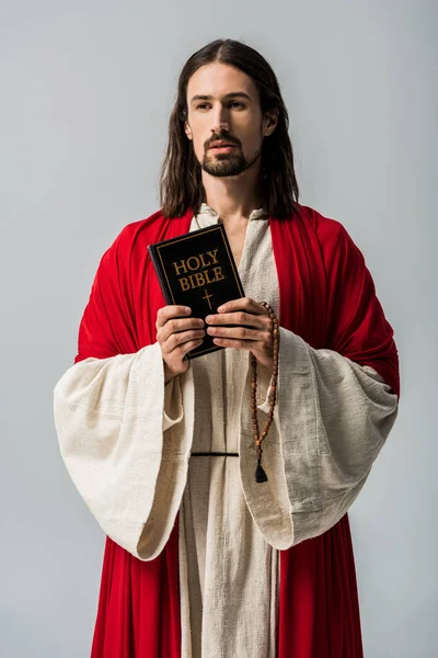 Handsome man holding rosary beads and holy bible isolated on grey — Stock Photo