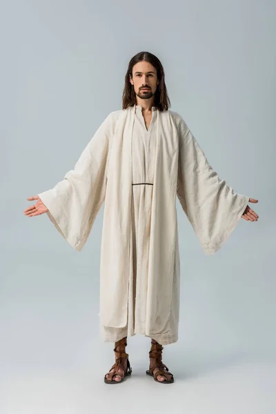 Красивий бородатий чоловік в халаті Ісуса, що стоїть з витягнутими руками на сірому — стокове фото