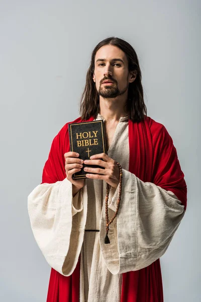 Man holding rosary beads and holy bible and looking at camera isolated on grey — Stock Photo