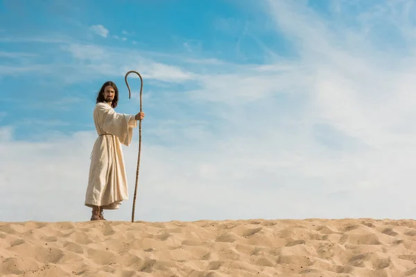Jesus holding wooden cane against blue sky in desert — Stock Photo