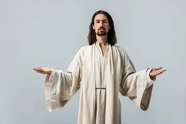 Hombre religioso mirando a la cámara y de pie con las manos extendidas aisladas en gris - foto de stock