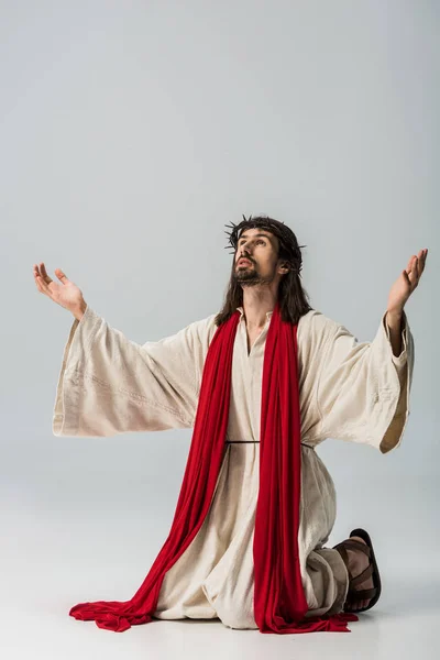 Бородатий чоловік у вінку молиться на колінах з витягнутими руками на сірому — стокове фото