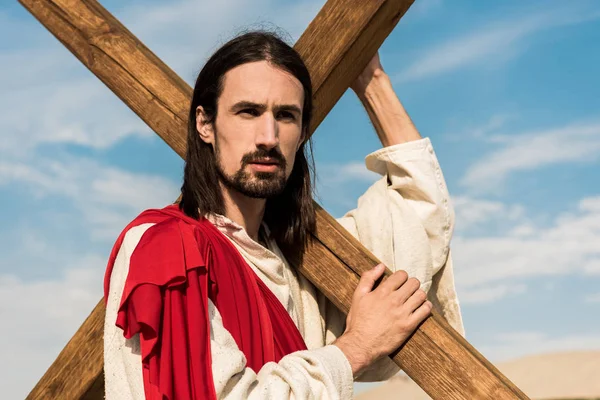 Бородатый человек держит деревянный крест против голубого неба — стоковое фото