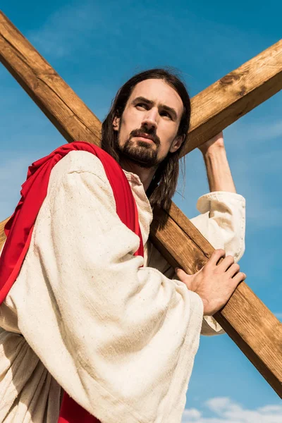 Vue à angle bas de Jésus tenant la croix contre le ciel bleu — Photo de stock