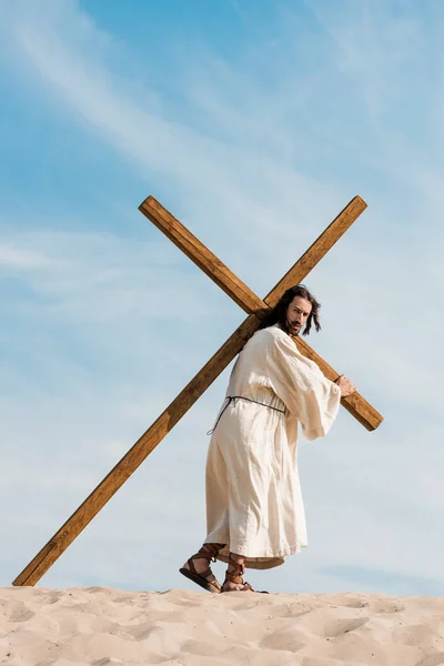 Jesus walking with wooden cross in desert — Stock Photo