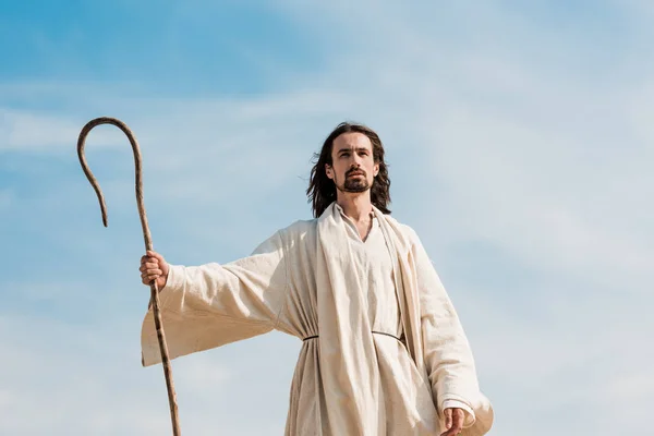 Jesus holding wooden cane against blue sky and clouds — Stock Photo