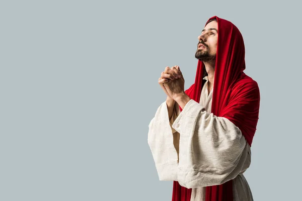 Красивый мужчина в красном капюшоне молится изолированно на сером — стоковое фото