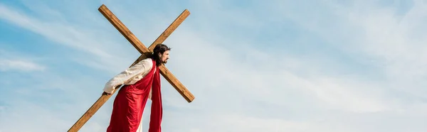 Panoramic shot of bearded man walking with wooden cross — Stock Photo