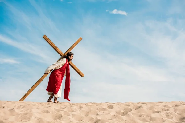 Hombre barbudo caminando con cruz de madera en el desierto - foto de stock