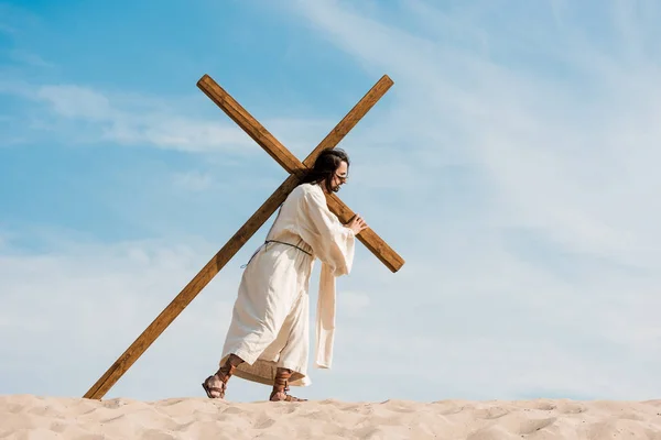 Бородатый человек идет с деревянным крестом против неба в пустыне — стоковое фото