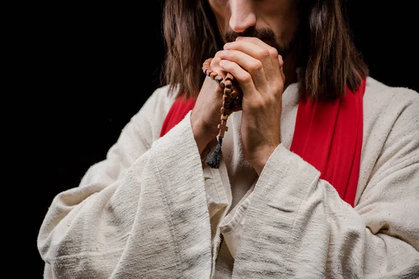 Cropped view of man holding rosary beads while praying isolated on black — Stock Photo