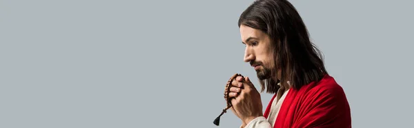 Panoramic shot of religious man holding rosary beads while praying isolated on grey — Stock Photo