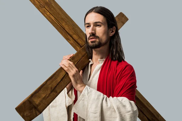 Красивый бородатый мужчина в халате Иисуса держит деревянный крест, изолированный на сером — стоковое фото