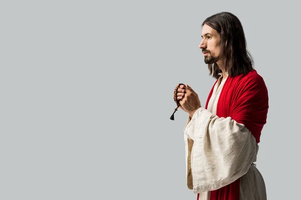 Jesús sosteniendo cuentas de rosario mientras rezaba aislado en gris - foto de stock