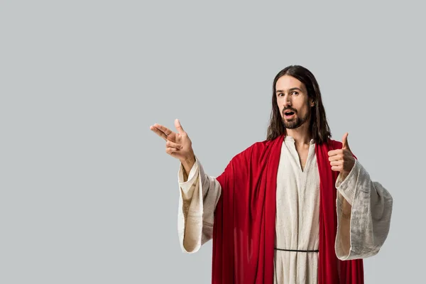 Удивленный человек в халате Иисуса показывает большой палец и жесты изолированы на сером — стоковое фото