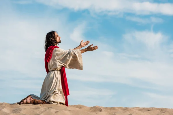 Jesus praying on knees on sand in desert against sky — Stock Photo