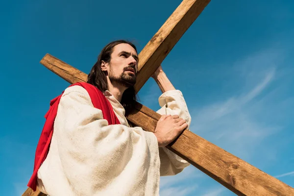Низький кут зору бородатого чоловіка з дерев'яним хрестом — стокове фото
