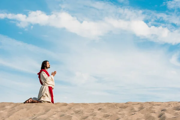 Uomo che prega in ginocchio nel deserto contro il cielo — Foto stock