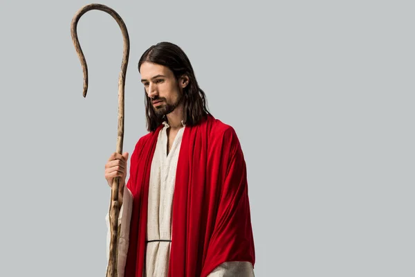 Грустный человек в халате Иисуса держа деревянную трость, изолированную на сером — стоковое фото