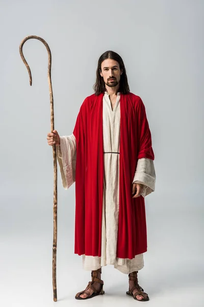 Handsome man in jesus robe holding wooden cane on grey — Stock Photo