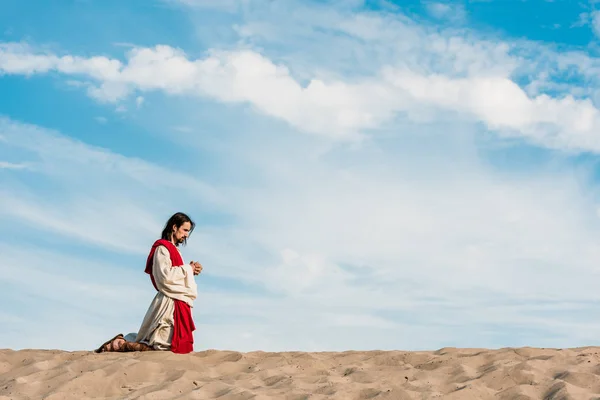 Man praying on knees with clenched hands in desert — Stock Photo