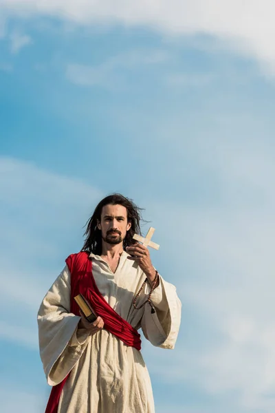 Jesus holding holy bible and cross against blue sky outside — Stock Photo