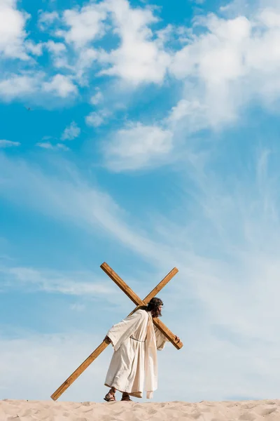Бородатий чоловік ходить з дерев'яним хрестом у пустелі на золотому піску — стокове фото