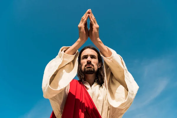 Low angle view of jesus with praying hands against blue sky — Stock Photo