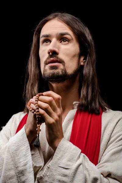 Bearded man praying while holding rosary beads isolated on black — Stock Photo