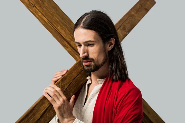 Грустный бородатый мужчина в одежде Иисуса держит деревянный крест изолированный на сером — стоковое фото