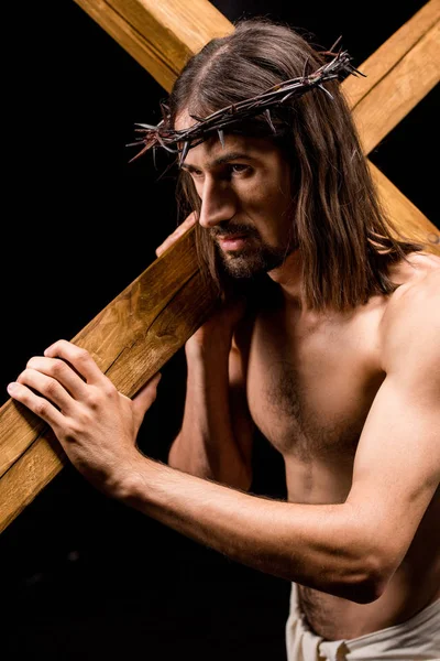 Jesus in wreath with spikes holding wooden cross isolated on black — Stock Photo