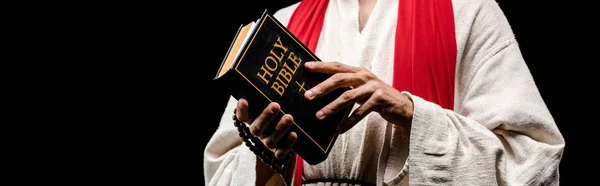 Panoramische Aufnahme eines Mannes, der ein Buch mit heiligen Bibelbuchstaben hält, isoliert auf schwarz — Stockfoto