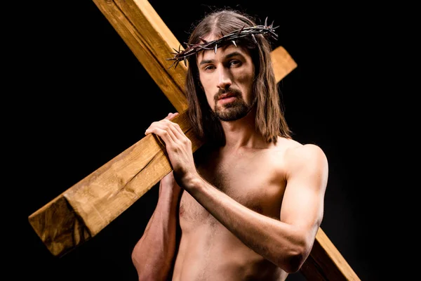 Hemdloser Mann im Kranz mit Spikes, die das Kreuz isoliert auf schwarz halten — Stockfoto