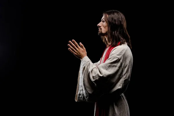 Vista lateral del hombre con las manos de oración aisladas en negro - foto de stock