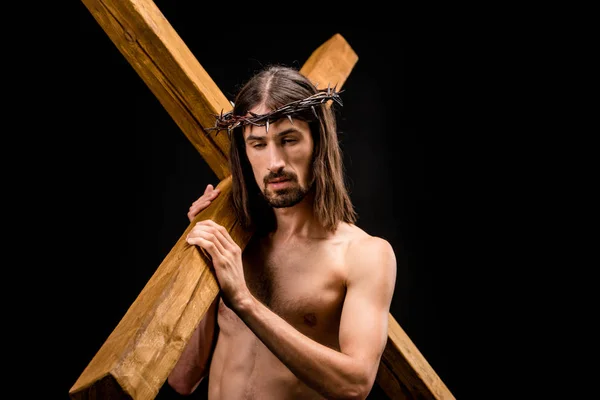 Triste hombre sin camisa en corona sosteniendo cruz aislado en negro - foto de stock