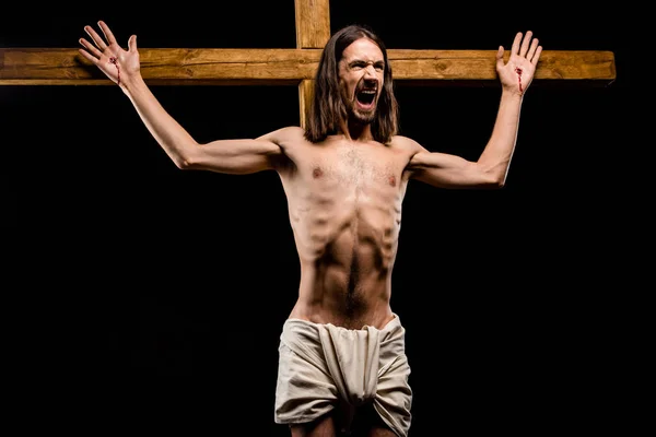 Shirtless man crucified on wooden cross screaming isolated on black — Stock Photo