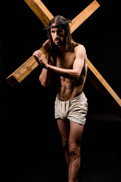 Hombre sin camisa barbuda en corona sosteniendo cruz de madera aislada en negro - foto de stock