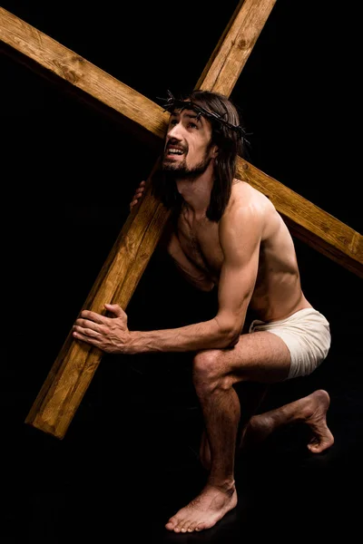 Jesus holding heavy wooden cross while sitting on black — Stock Photo