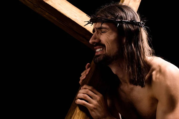 Jesus mit geschlossenen Augen hält schweres Holzkreuz isoliert auf schwarz — Stockfoto