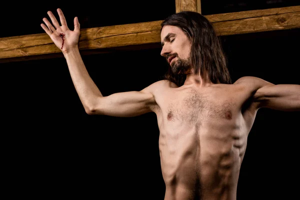Jesús con los ojos cerrados crucificado en la cruz de madera aislado en negro - foto de stock