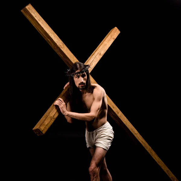 Jesus in wreath holding wooden cross and standing isolated on black — Stock Photo