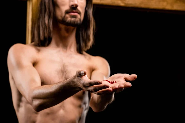 Cropped view of jesus with cupped hands near wooden cross isolated on black — Stock Photo
