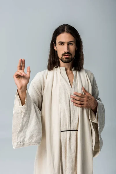 Schöner Mann im Jesusgewand mit der Hand auf der Brust gestikulierend isoliert auf grau — Stockfoto