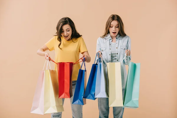 Attractive and shocked friends holding shopping bags isolated on beige — Stock Photo