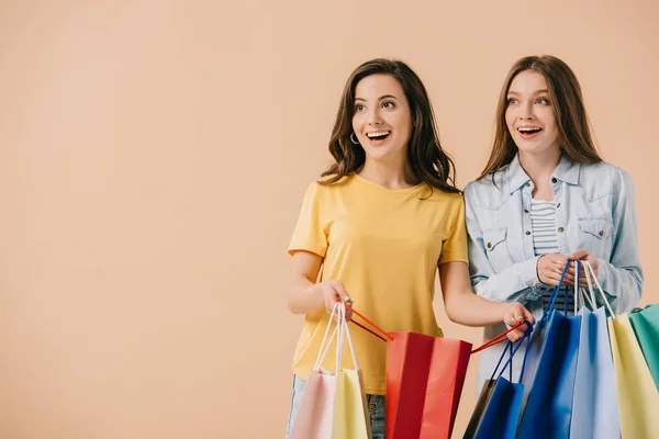 Attractive and smiling friends holding shopping bags isolated on beige — Stock Photo