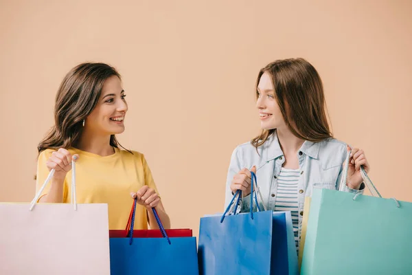 Amis attrayants et souriants tenant des sacs à provisions isolés sur beige — Photo de stock